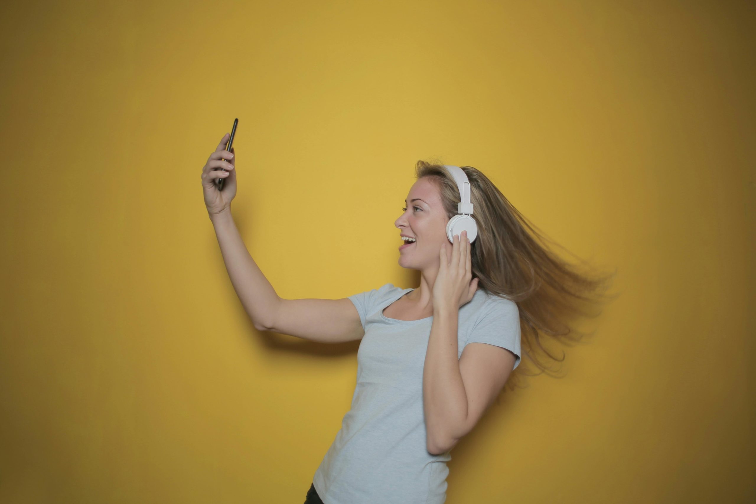 Seitenansicht Foto Der Lächelnden Frau Im Weißen Trägershirt, Das Musik Auf Kopfhörern Hört, Während Sie Ein Selfie Nimmt