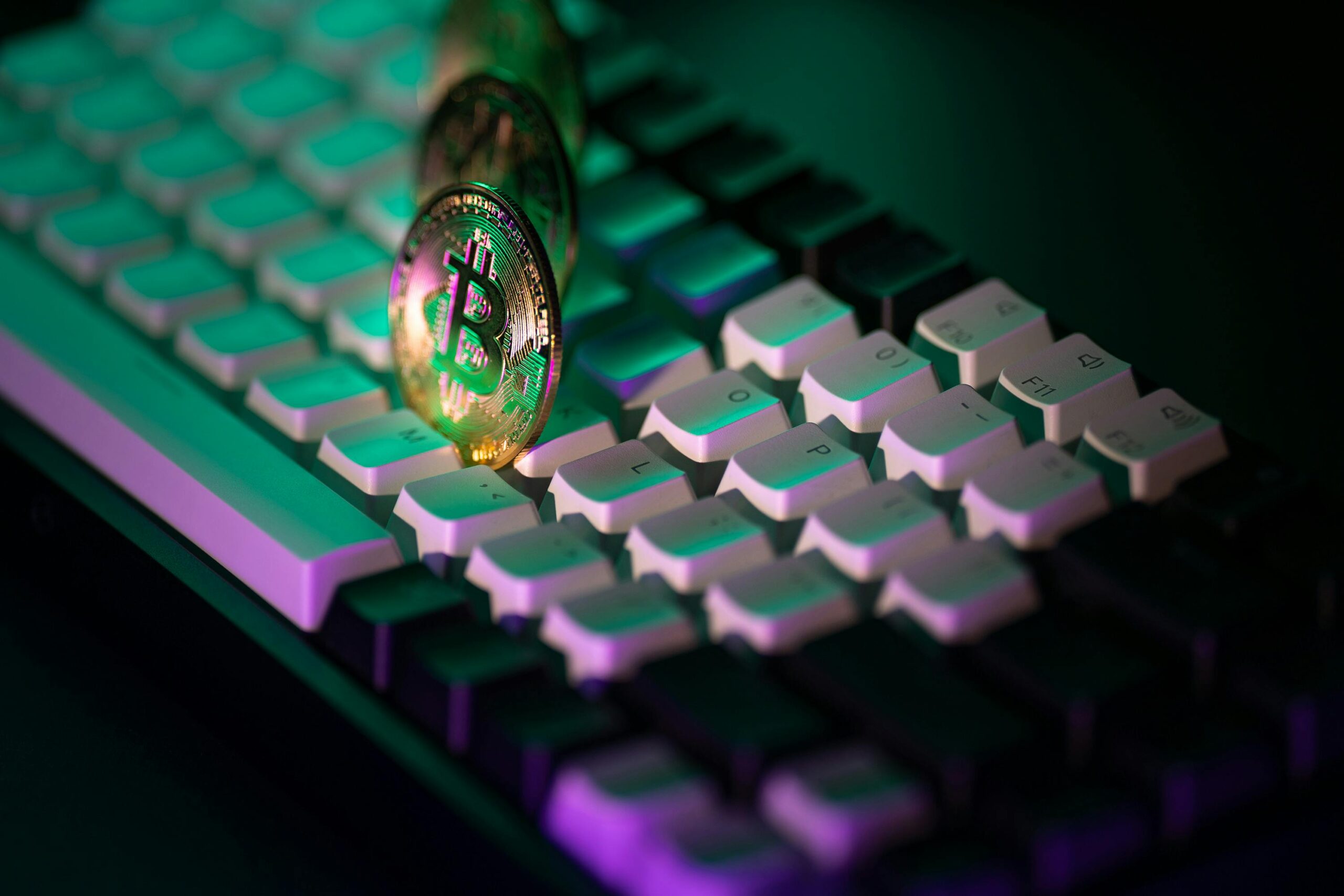Goldene Bitcoin-Münzen auf einer Tastatur mit bunter Neonbeleuchtung. Modernes Kryptowährungskonzept.