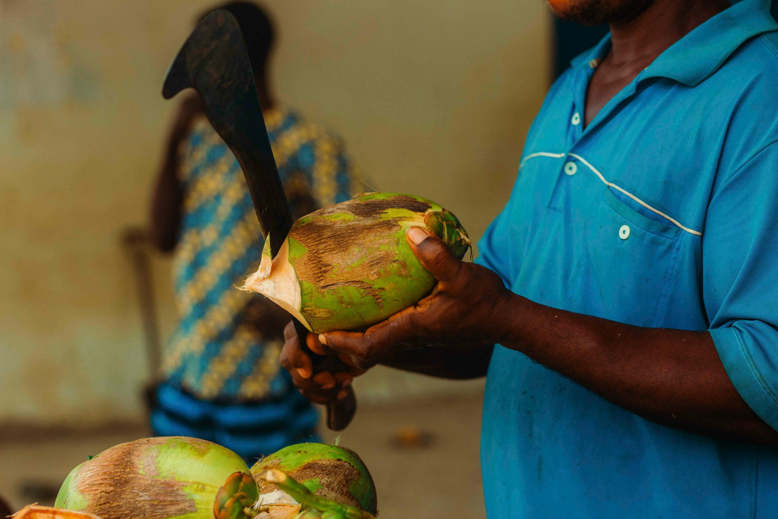 Hände schneiden auf einem lebhaften ghanaischen Markt frische Kokosnüsse und zeigen die traditionelle Zubereitung von Speisen.