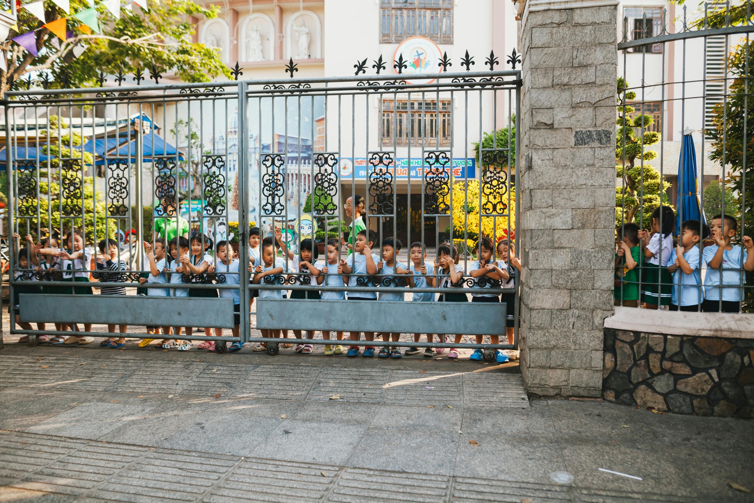 Eine Gruppe kleiner Kinder steht in einer Reihe und späht durch ein dekoratives Schultor, während sie einen sonnigen Tag im Freien genießen.