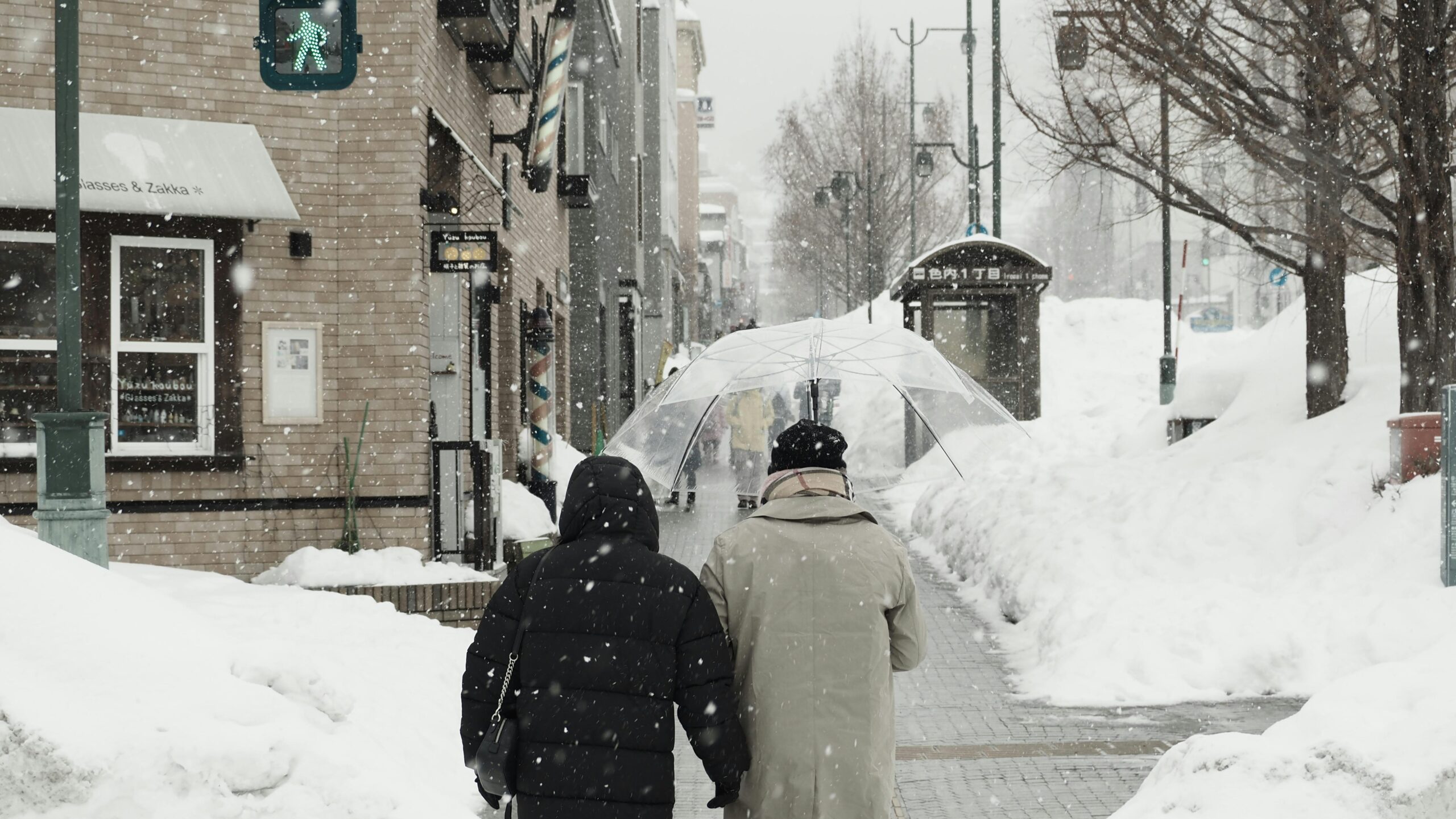 Verschneite Straßenszene in Sapporo, Hokkaido, Japan, mit Menschen, die unter Regenschirmen spazieren.
