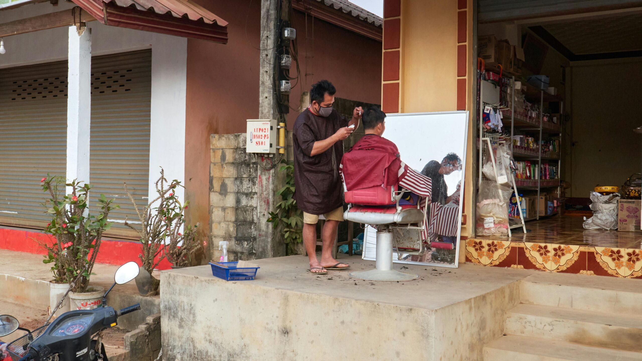 Traditioneller Haarschnitt im Freien in einem ländlichen Dorf in Laos, der den lokalen Lebensstil zeigt.