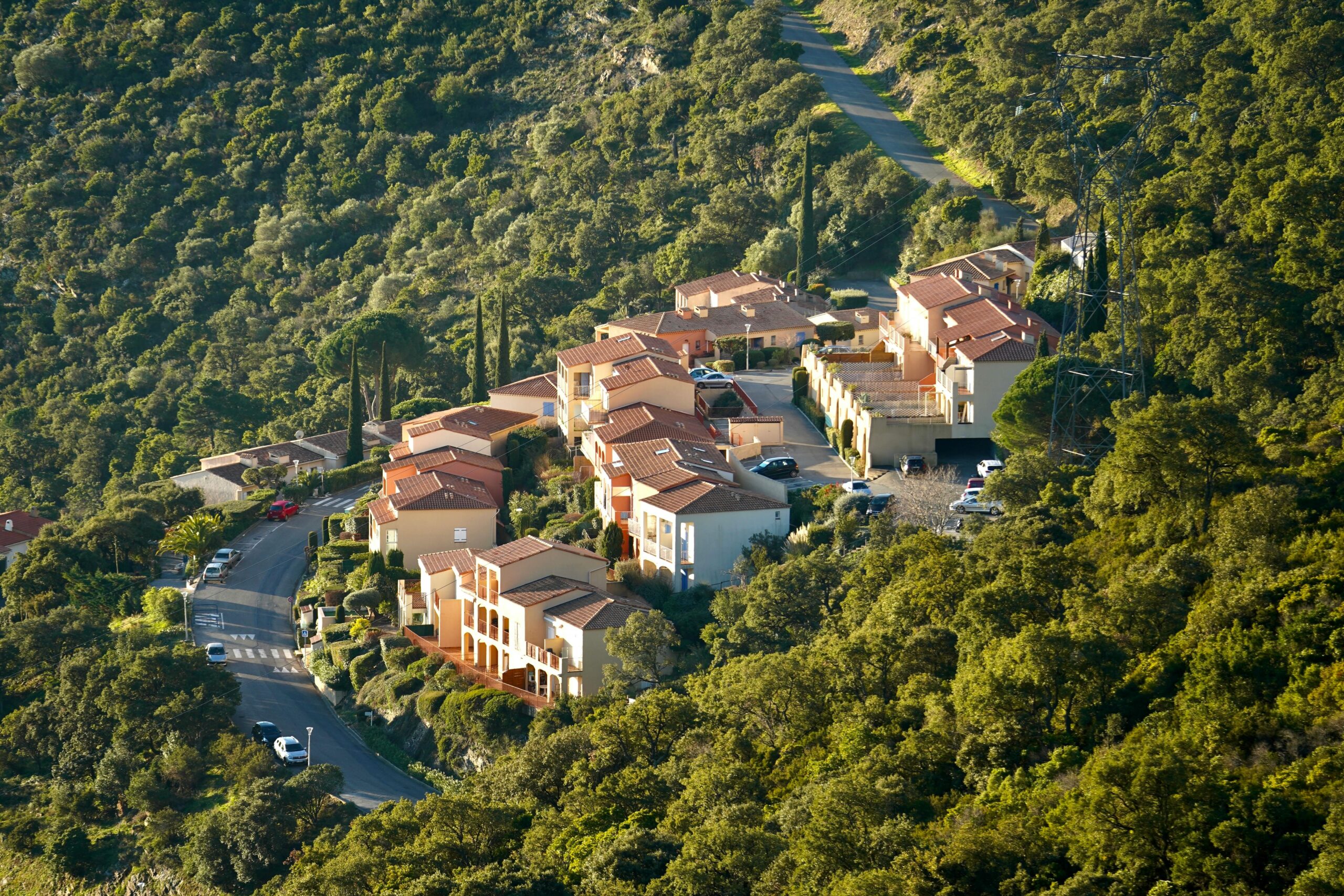 Luftaufnahme eines malerischen mediterranen Dorfes, eingebettet in eine üppige Waldlandschaft, in Tageslicht getaucht.